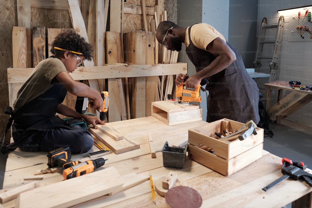 Retrato com vista lateral de pai e filho afro-americanos trabalhando juntos na oficina de carpintaria
