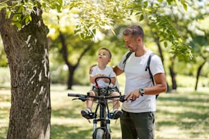 A puzzled son looking at the tree and sitting on a bike while father explaining him photosynthesis.