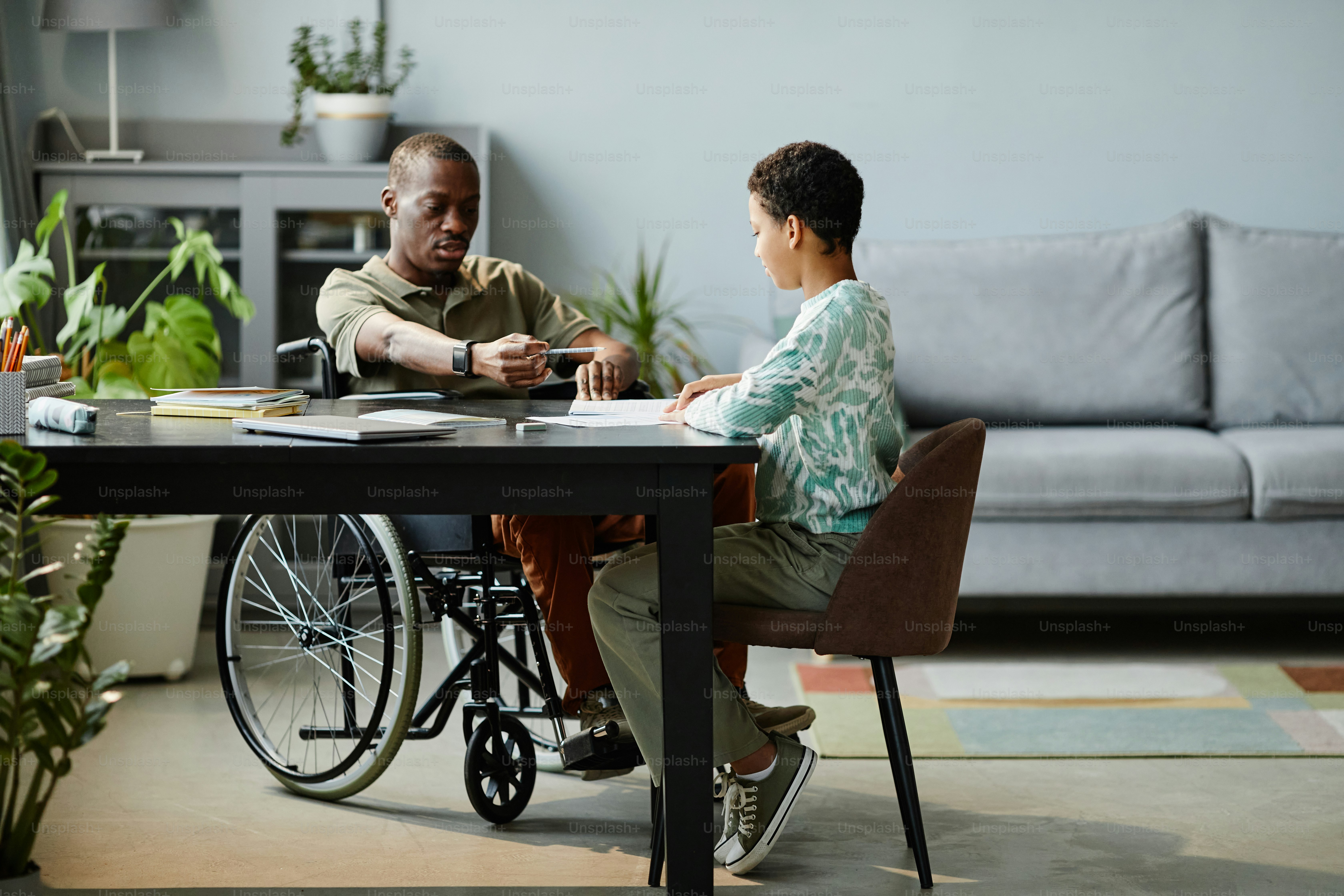Full length portrait of father with disability helping daughter studying at home, copy space