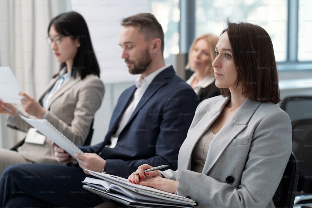 Group of young contemporary economists sitting in front of speaker during presentation of company income fluctuation