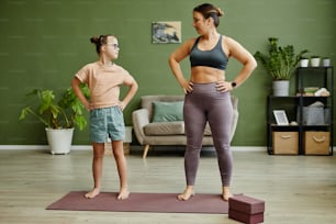Full length portrait of young female instructor assisting girl with down syndrome exercising in fitness studio, copy space
