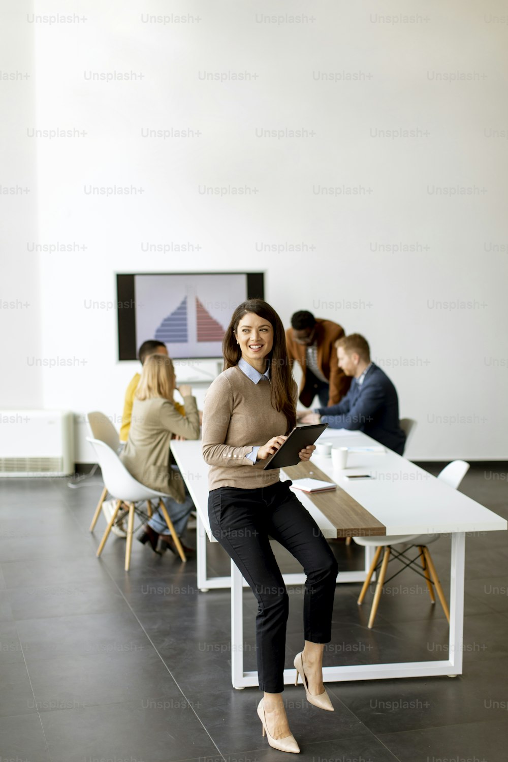 Mignonne jeune femme d’affaires debout dans le bureau et utilisant une tablette numérique devant son équipe