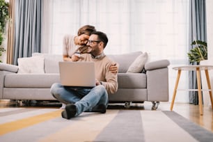 A couple in love embraces and uses a credit card for e-shopping at home.