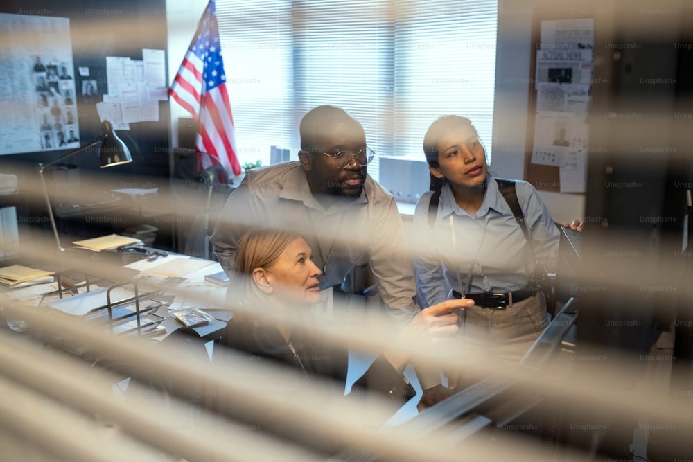 Eine Gruppe von FBI-Agenten in formeller Kleidung diskutiert über das Verhalten von Kriminellen, während sie die Aufzeichnung der Überwachungskamera im Büro beobachtet