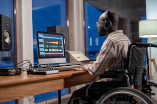 Young serious African American musician with disability looking at computer screen with sound visualization in studio