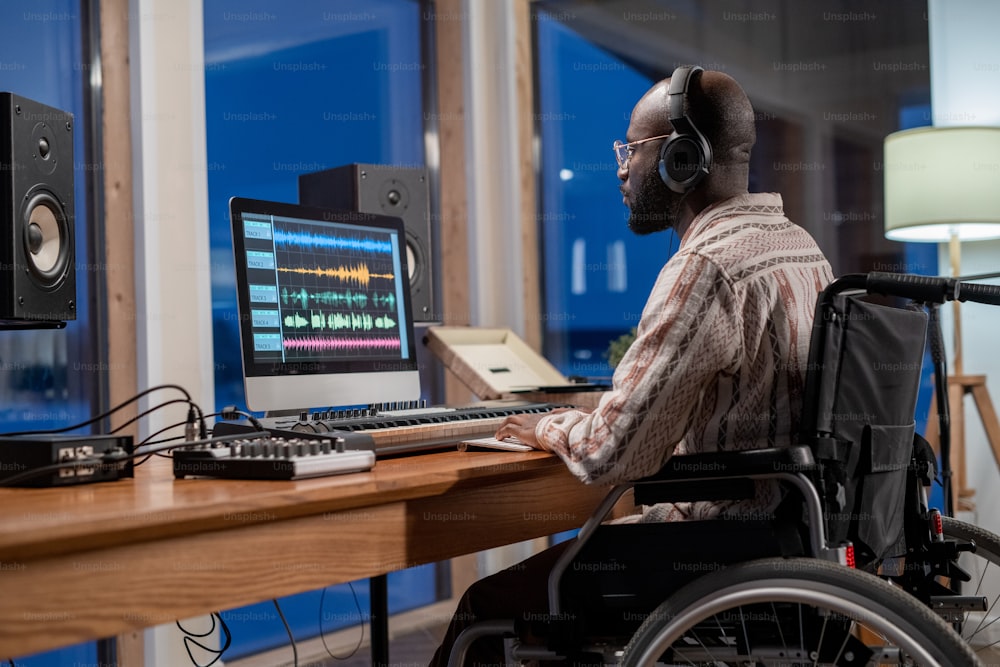 障害を持つ若い真面目なアフリカ系アメリカ人ミュージシャンが、スタジオで音の視覚化でコンピューター画面を見ている