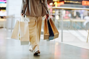 Section basse d’une femme méconnaissable portant un pantalon et tenant des sacs à provisions vierges tout en marchant dans le centre commercial, espace de copie