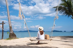 海辺の木製のブランコに座ってくつろぐ美しいアジアの若い女性の背面図画像
