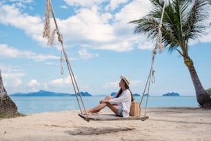 Portrait image of a beautiful young asian woman sitting on wooden swing by the sea