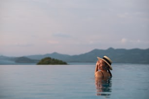 Una mujer joven relajándose en una piscina infinita con una hermosa vista al mar