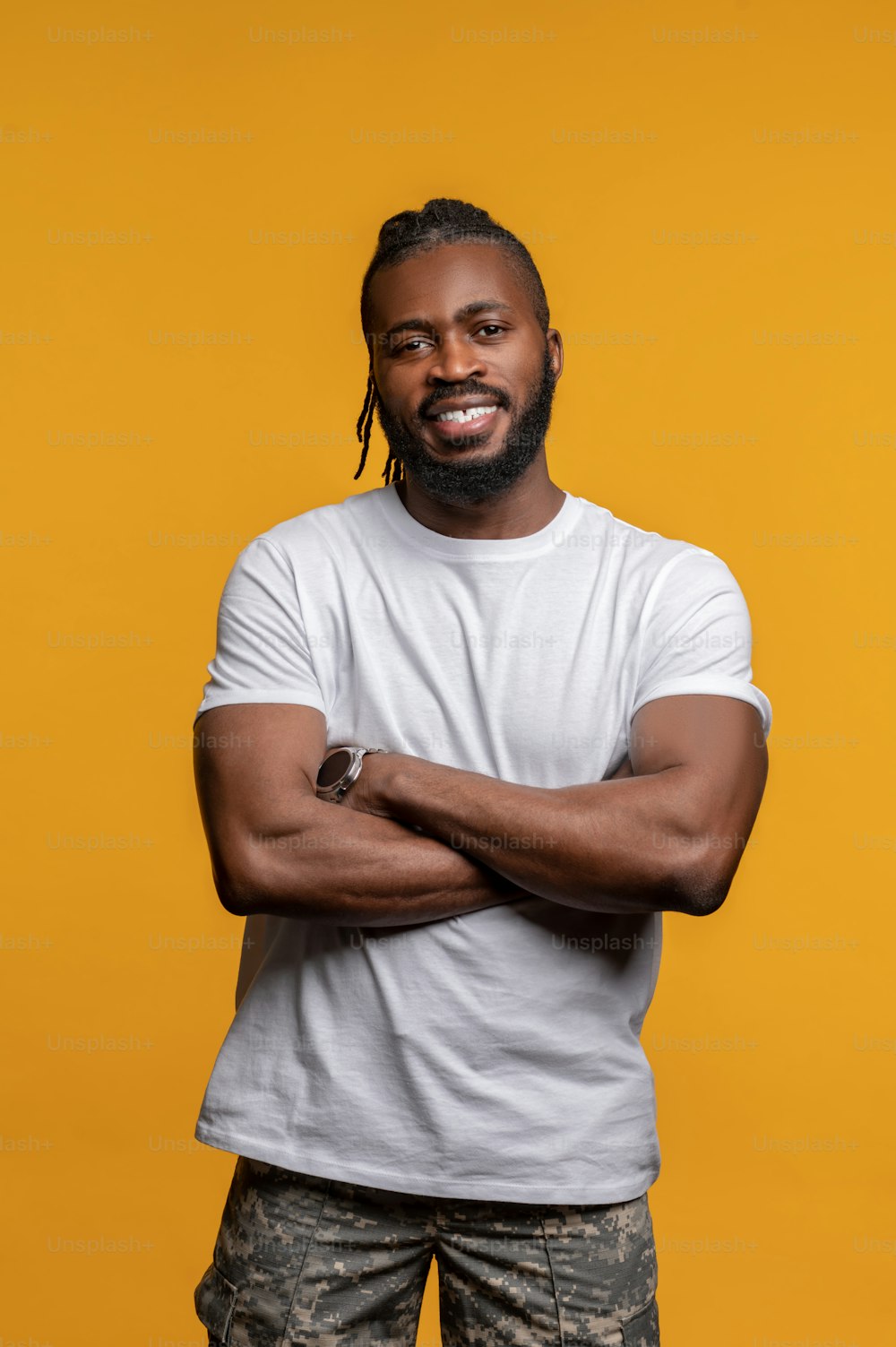 Front view of a cheerful fit guy with his arms folded posing for the camera against the yellow background