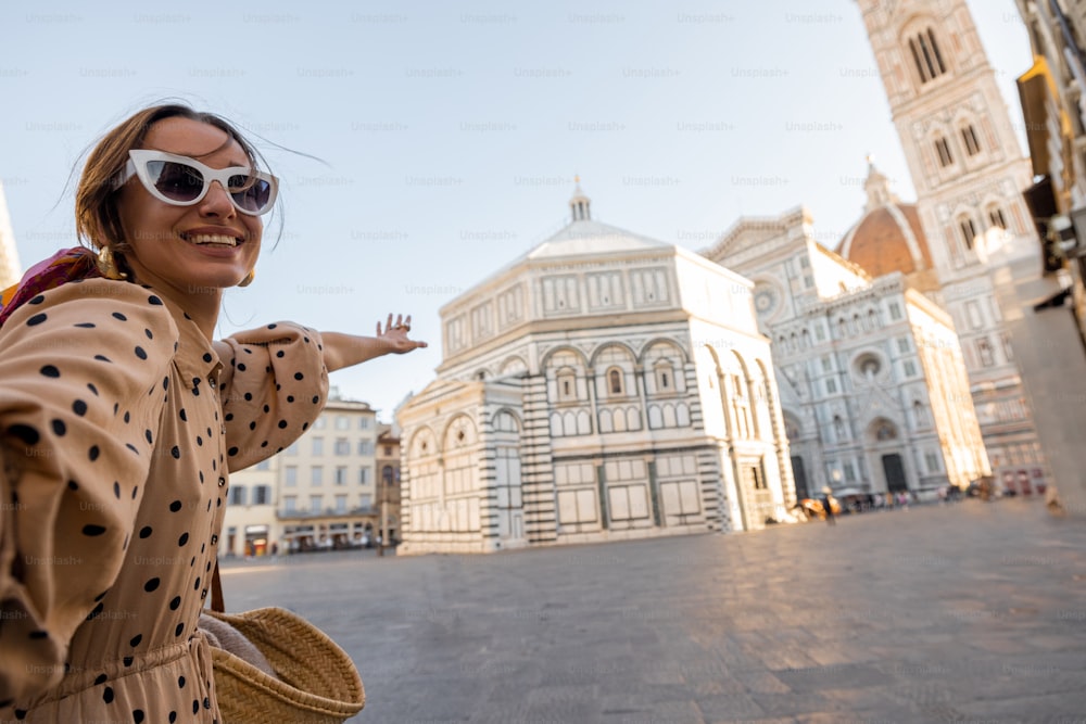 Woman takes selfie photo in front of famous Duomo cathedral in Florence, standing on empty cathedral square during morning time. Stylish woman visiting italian landmarks. Traveling Italy concept