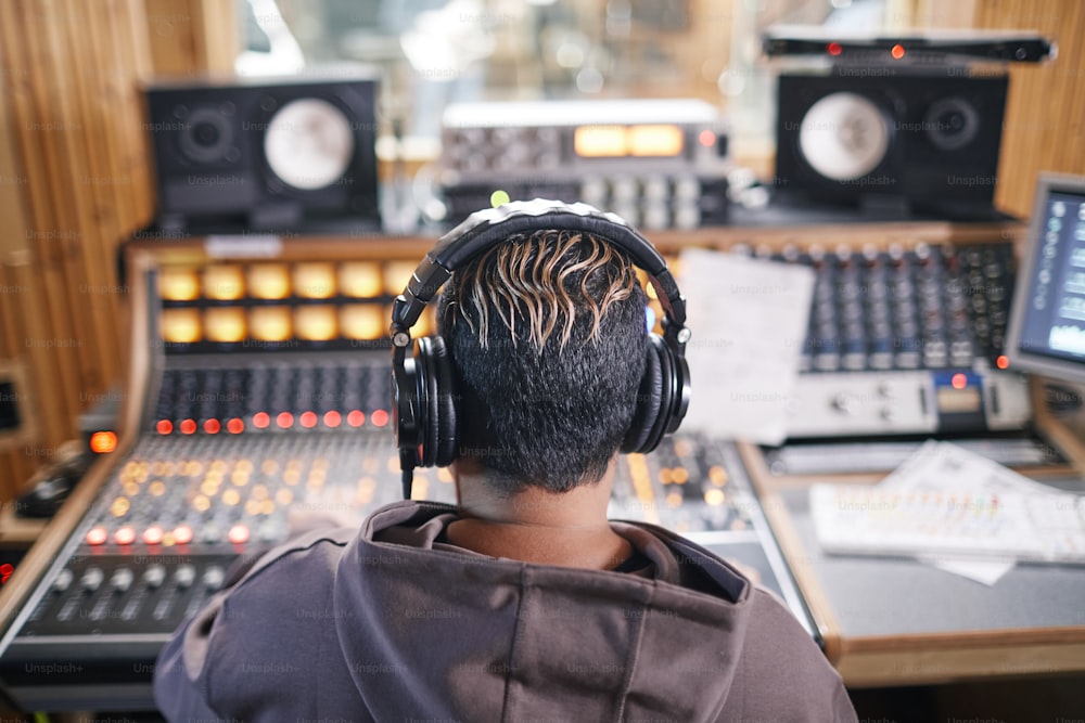 Vista traseira em músico jovem anônimo usando fones de ouvido em estúdio de gravação profissional, espaço de cópia