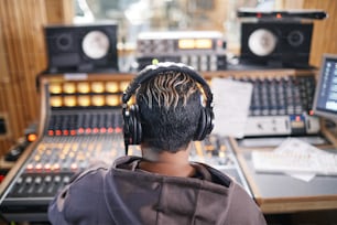Back view at anonymous young musician wearing headphones in professional recording studio, copy space