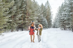 Feliz hombre afroamericano, su esposa y su hijo paseando al aire libre en un helado día de invierno entre coníferas cubiertas de nieve