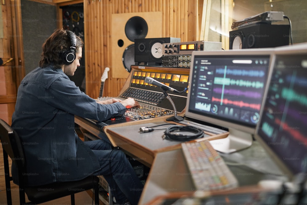 Grande angular no produtor musical operando estação de trabalho de áudio em estúdio de gravação profissional, espaço de cópia