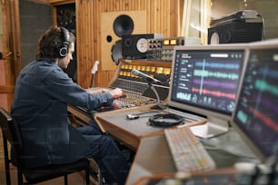 Wide angle at music producer operating audio workstation in professional recording studio, copy space