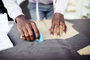 Close-up image of tailor tracing sewing pattern on fabric with blue chalk