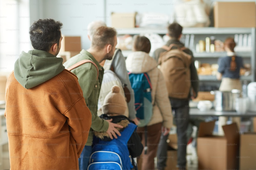 Background image of Caucasian refugees in line at donation center, focus on young child with backpack, copy space