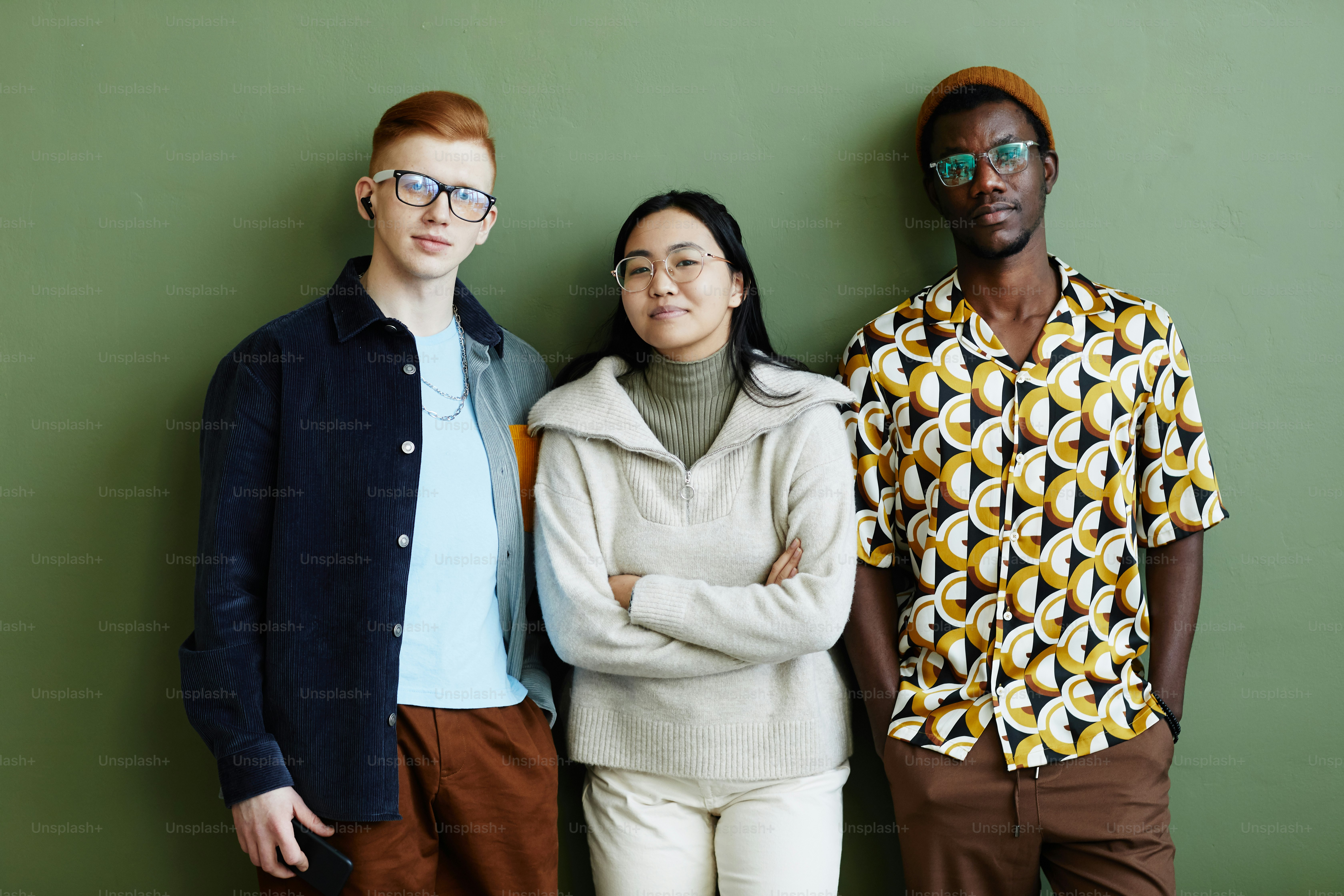 Minimal portrait of diverse creative team looking at camera while standing against green wall in office