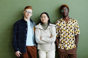 Minimal portrait of diverse creative team looking at camera while standing against green wall in office