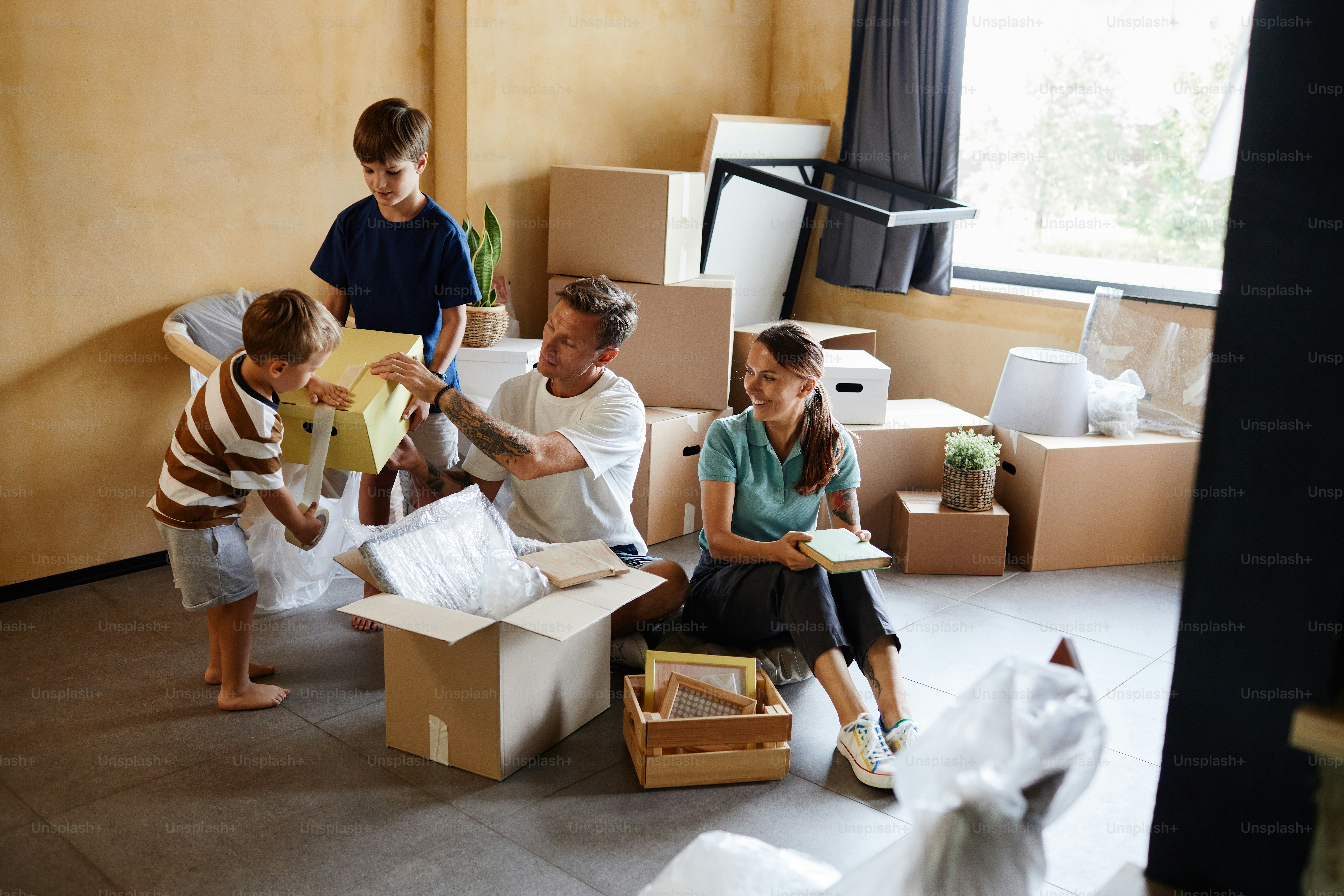 Full length portrait of happy family with two children unpacking boxes together while moving house, copy space
