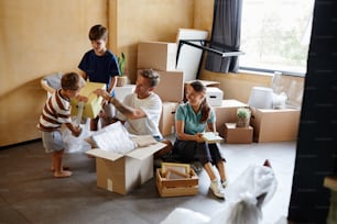 Ritratto a figura intera della famiglia felice con due bambini che disimballano le scatole insieme durante il trasloco, lo spazio della copia
