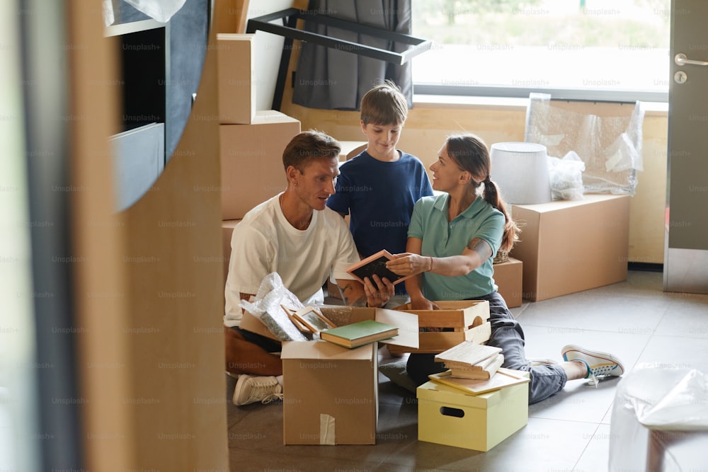 Portrait candide d’une famille heureuse déballant des boîtes assises par terre tout en emménageant dans une nouvelle maison, espace de copie