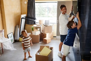 Retrato de vista lateral de padre e hijo sonrientes colgando la televisión en la pared juntos mientras se mudan a una nueva casa, copie el espacio