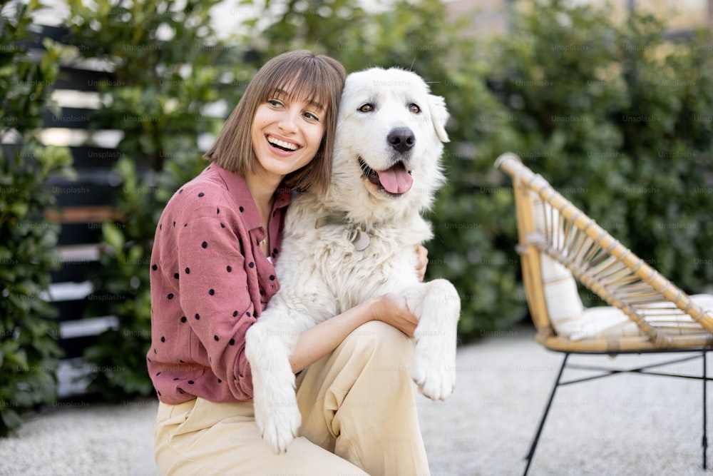 Portrait of a woman hugs with her adorable white dog at backyard outdoors. Concept of friendship with pets and spending happy summer time outdoors. Maremma sheepdog