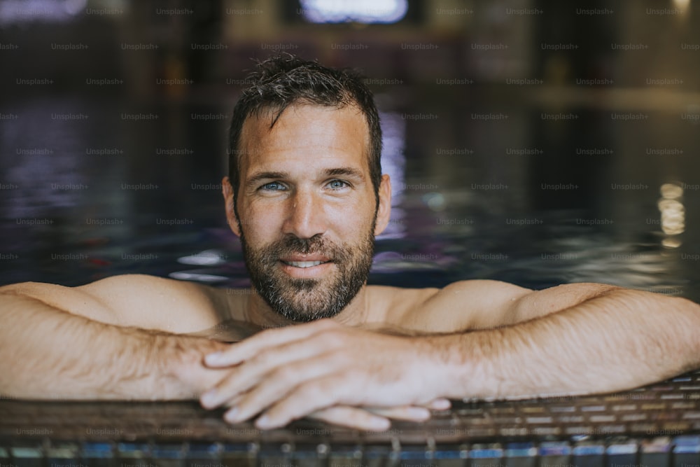 Portrait of handsome smiling young man relaxing by the swimming pool edge