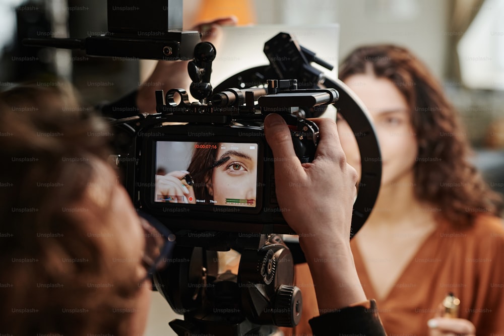 Screen of video camera with part of face of fashion model applying new volume mascara on eyelashes during commercial shooting