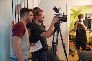 Jovem cinegrafista ou cinegrafista ajustando o foco da câmera antes de filmar anúncio ou evento em estúdio ou apartamento