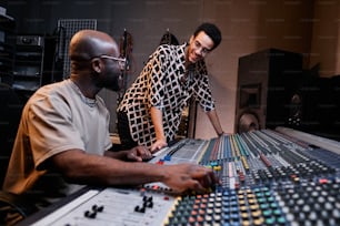 Maturo produttore musicale afroamericano e giovane cantante che chiacchiera di qualcosa di divertente mentre lavora in studio di registrazione