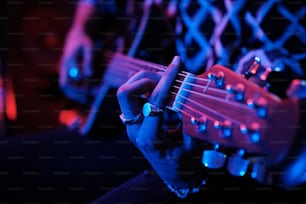 네온 불빛에서 어쿠스틱 기타를 연주하는 알아볼 수 없는 젊은 남성 음악가의 중간 클로즈업 샷