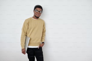 Young contemporary programmer or student in casualwear holding laptop while standing by wall of office and looking at camera