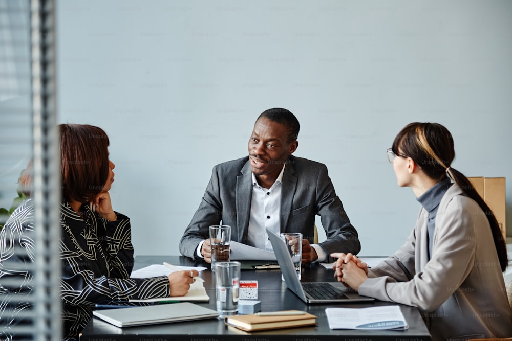 Portrait d’un jeune homme d’affaires noir parlant à l’équipe lors d’une réunion dans un bureau contre un mur bleu pâle, espace de copie