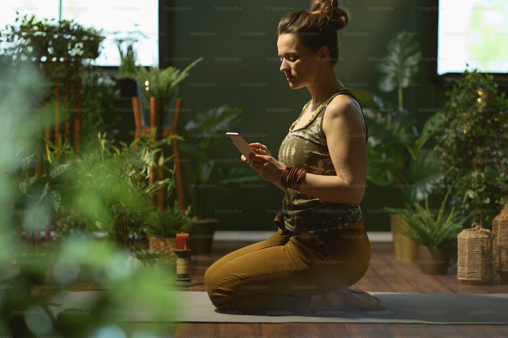 Donna elegante nel moderno salotto verde facendo yoga e usando lo smartphone.