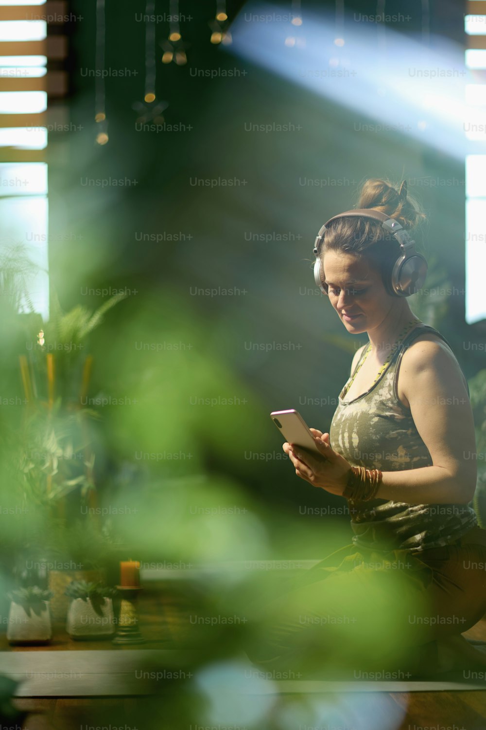 Mujer moderna de mediana edad con teléfono inteligente y auriculares en la moderna sala de estar verde.