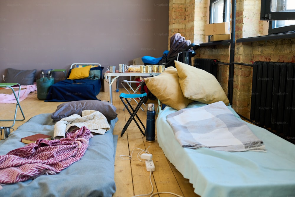 임시 노숙자를 위해 준비된 넓은 방에 담요 또는 격자 무늬로 만든 매트리스가있는 난민의 수면 공간 2 개