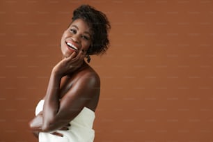 Portrait of happy excited young Black woman with beautiful toothy smile standing against brown background
