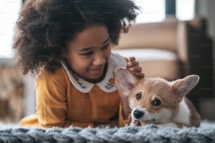 Amigos. Uma menina de cabelos cacheados em vestido laranja brincando com um filhote de cachorro
