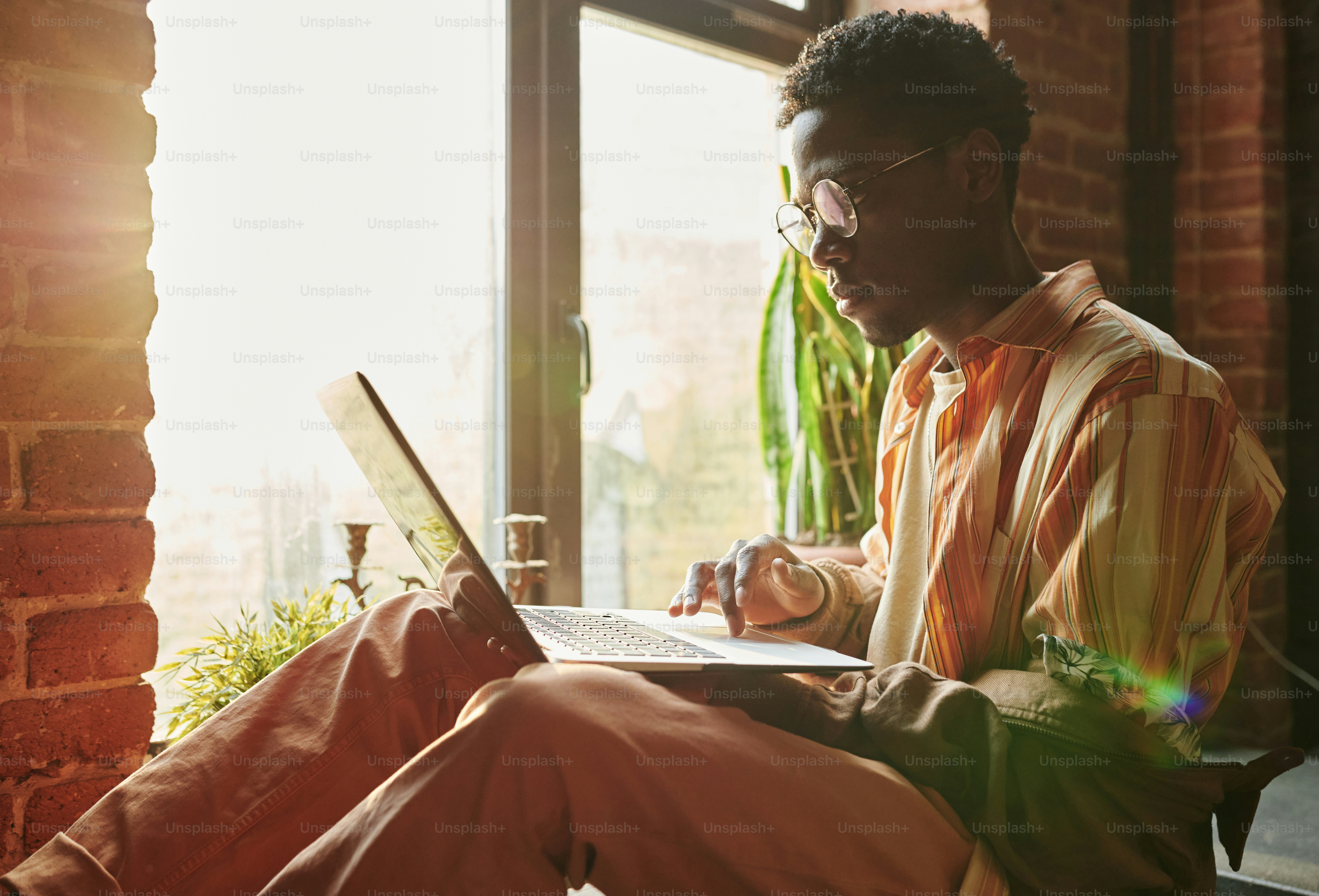 Side view of young black man looking at laptop screen while sitting ...