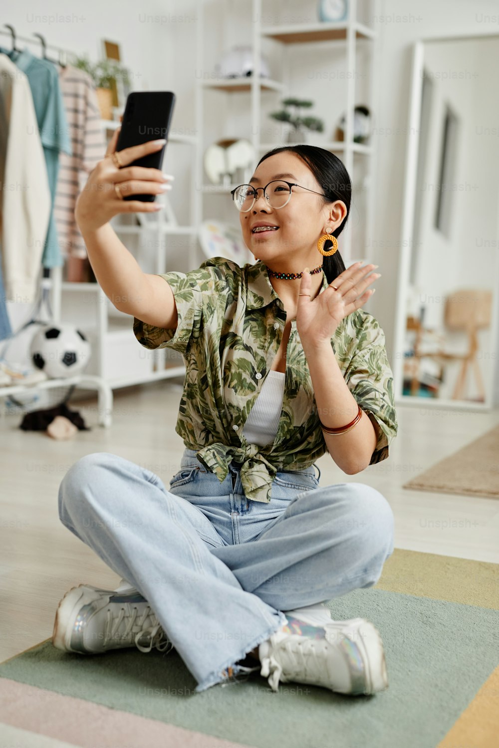 Ritratto verticale a figura intera di giovane adolescente che filma la storia per i social media mentre è seduta sul pavimento di casa