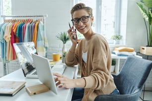 Happy young woman talking on mobile phone while working in fashion store office