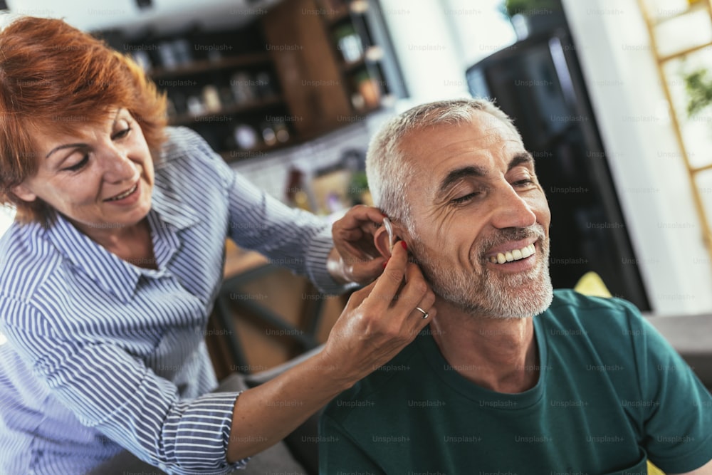 La mujer ayuda a un paciente masculino maduro a usar audífonos.