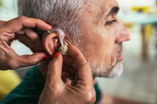 Woman helps mature male patient to use hearing aid.