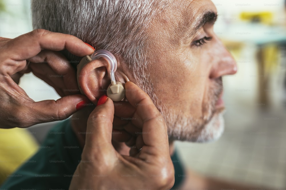 Mulher ajuda paciente maduro do sexo masculino a usar aparelho auditivo.