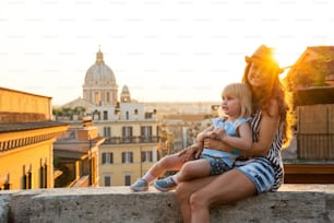 해질녘 로마의 옥상이 내려다보이는 거리에 앉아 있는 엄마와 아기 소녀