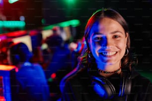 Ritratto ravvicinato di giovane donna sulla squadra di e-sport che sorride alla fotocamera allegramente illuminata dalla luce al neon, spazio di copia
